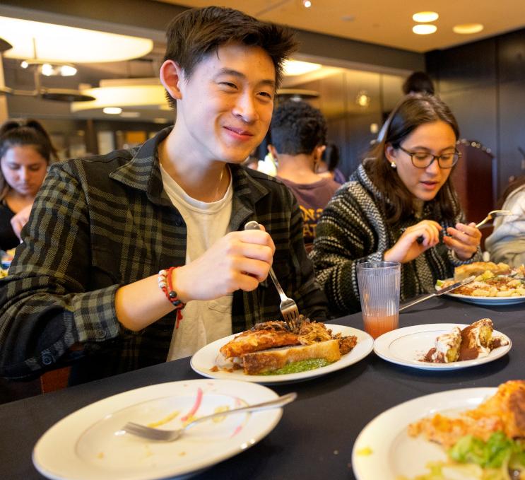 students sitting at a dining hall table eating a meal