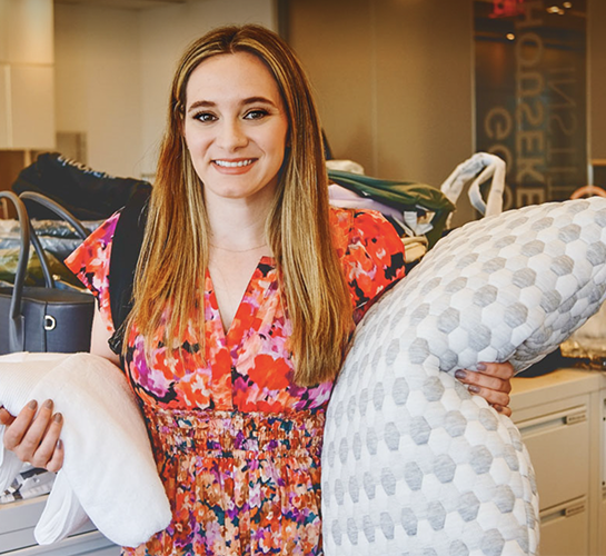 woman in a red floral dress holding a pillow and some textiles