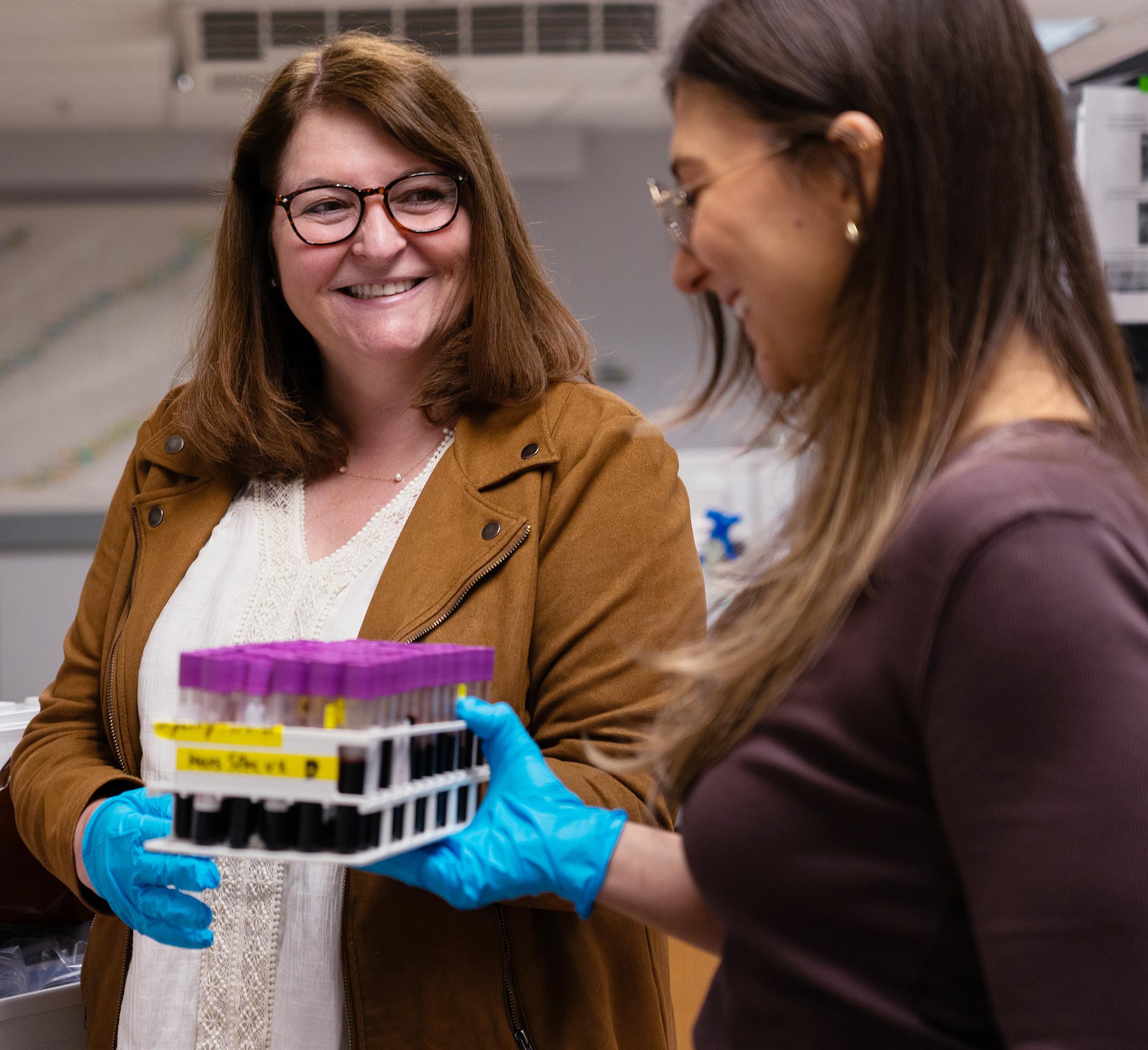 woman in glasses receives a tray of vials from a student in a research lab
