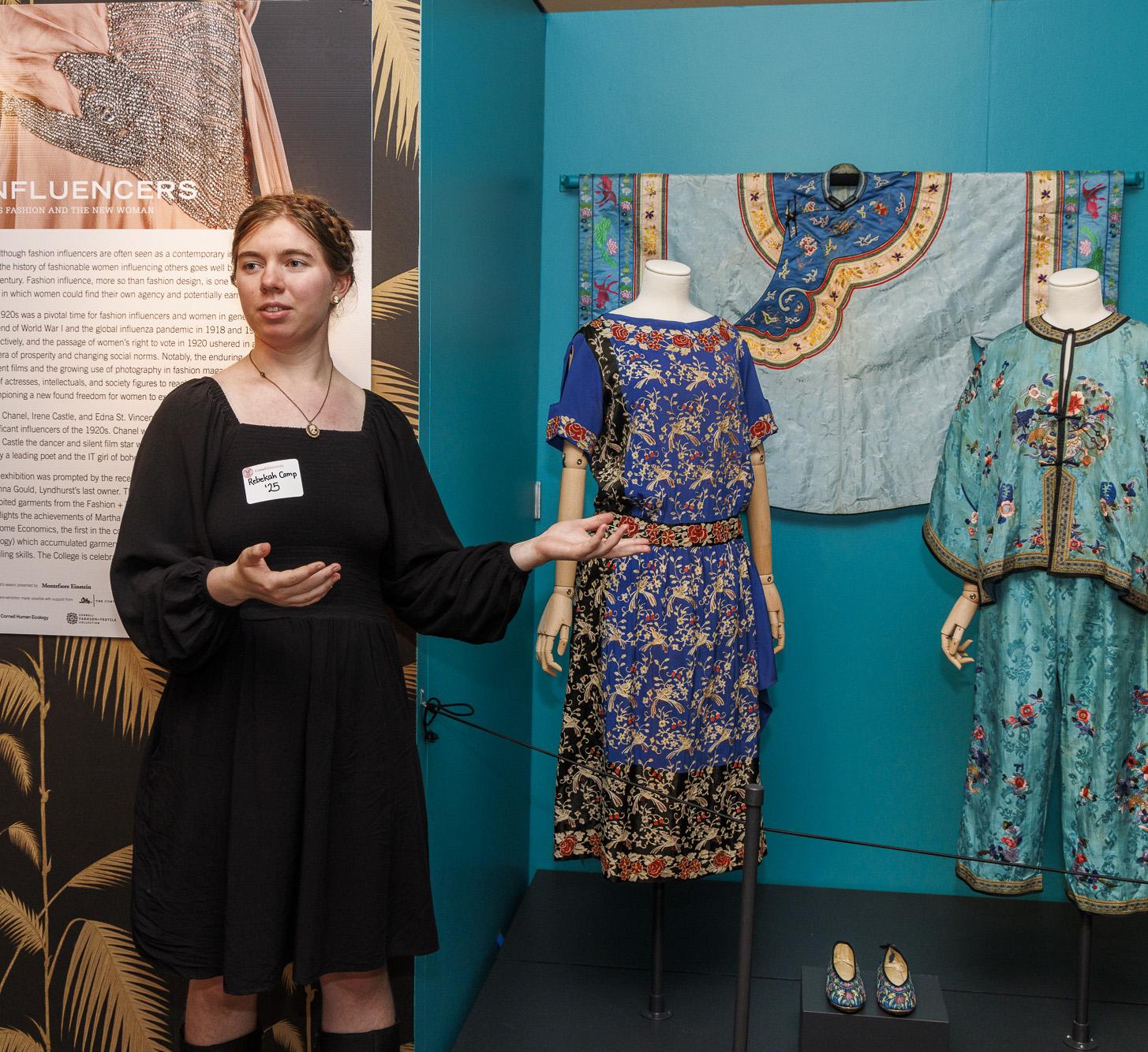 student gestures at some vintage dresses on mannequins in an exhibition