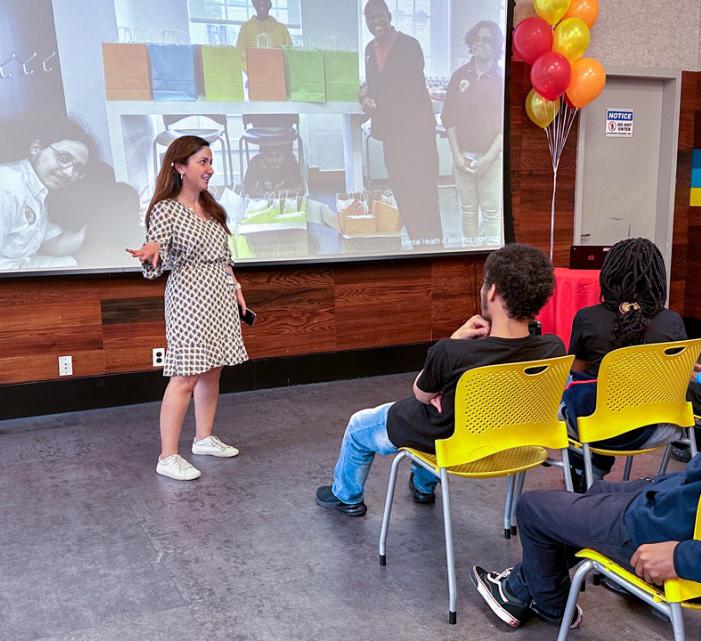 young woman speaking in front of youth seated in yellow chairs