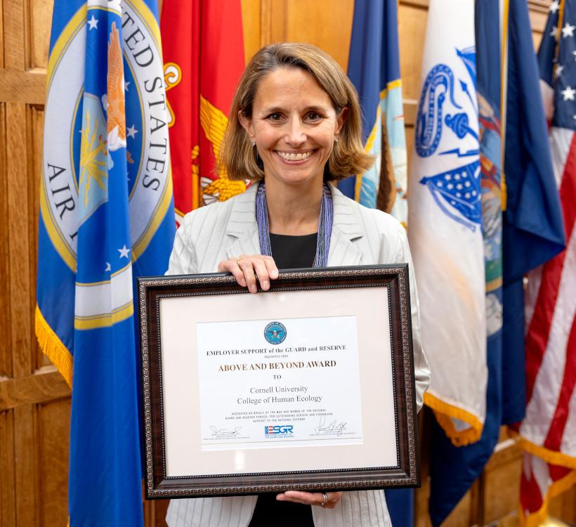 woman holding a framed certificate with a group of flags behind her