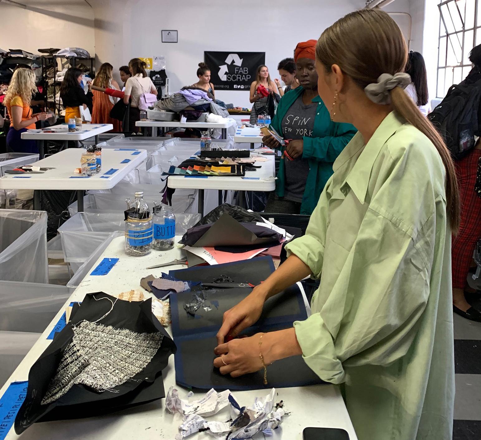 People working with piles of fabric on tables 