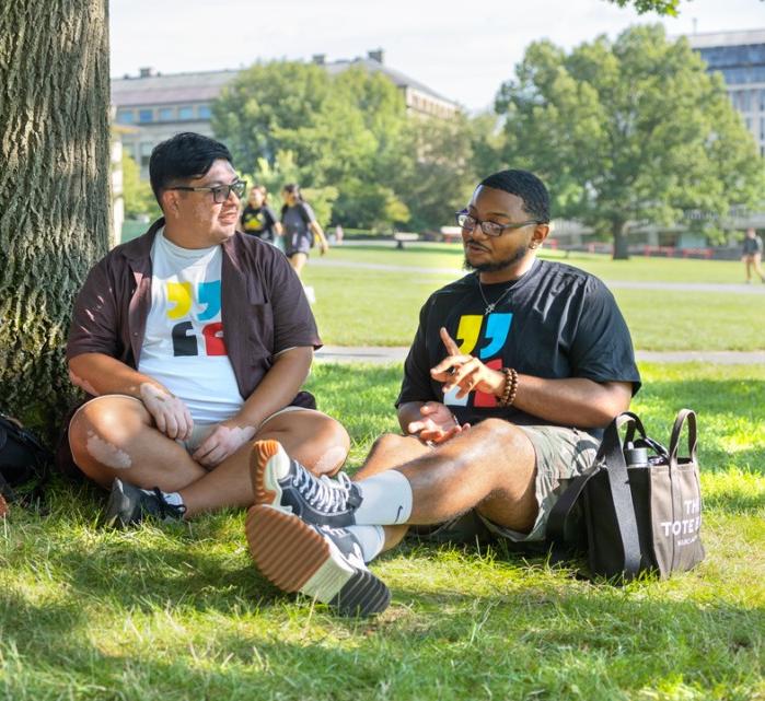 Two students sit and talk in the arts quad with freed of expression theme year tshirts on