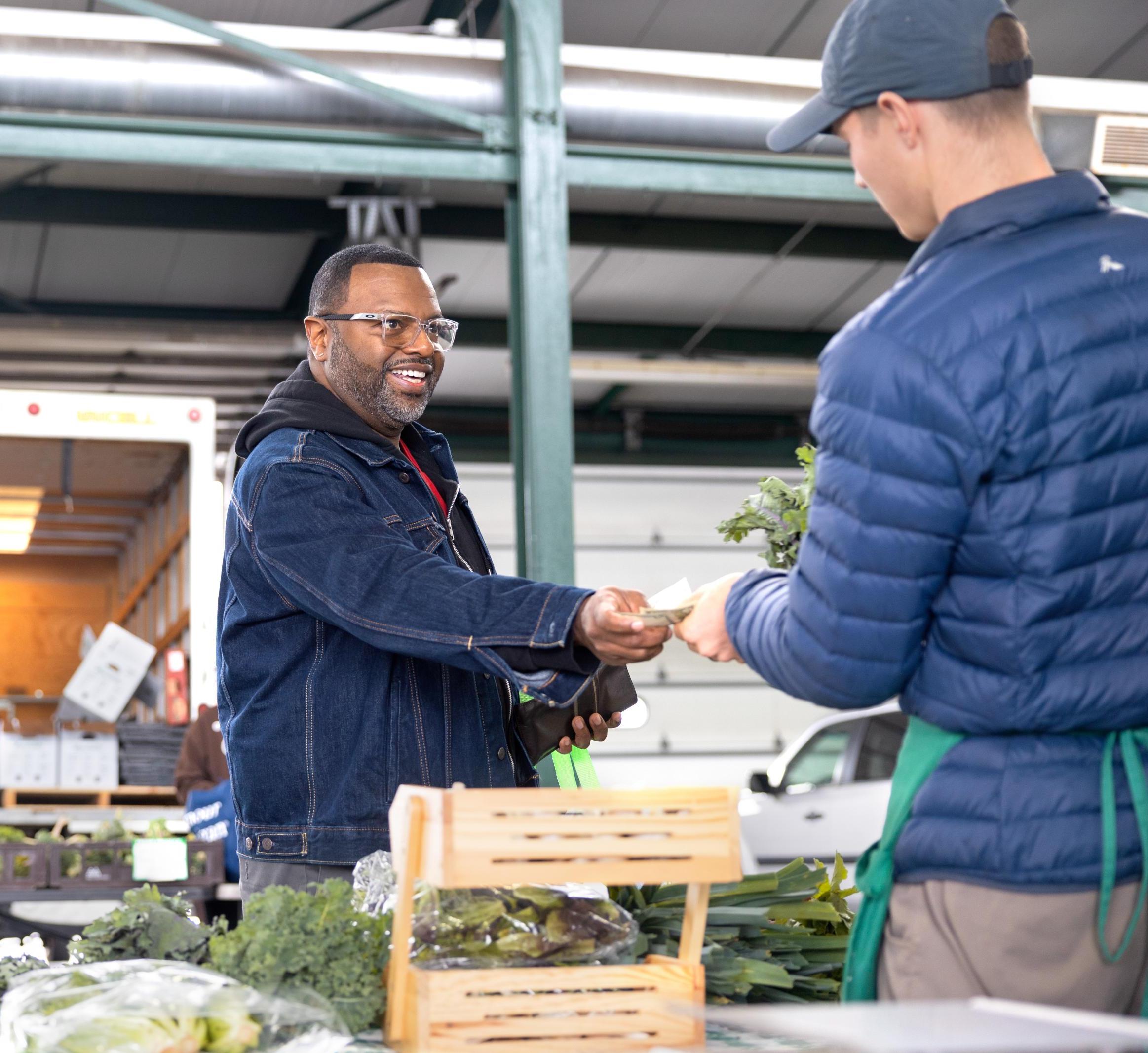 A person hands a SNAP coupon to a farmer