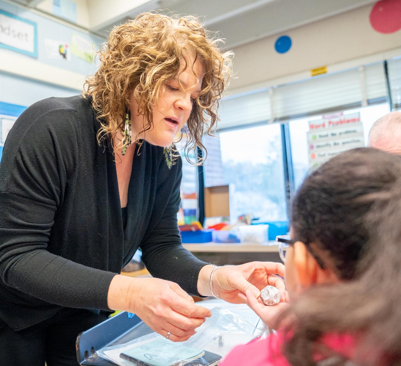 woman leans to talk to elementary school children in a classroom