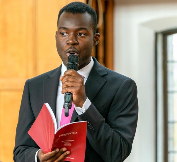 a student speaks into a microphone holding a red booklet