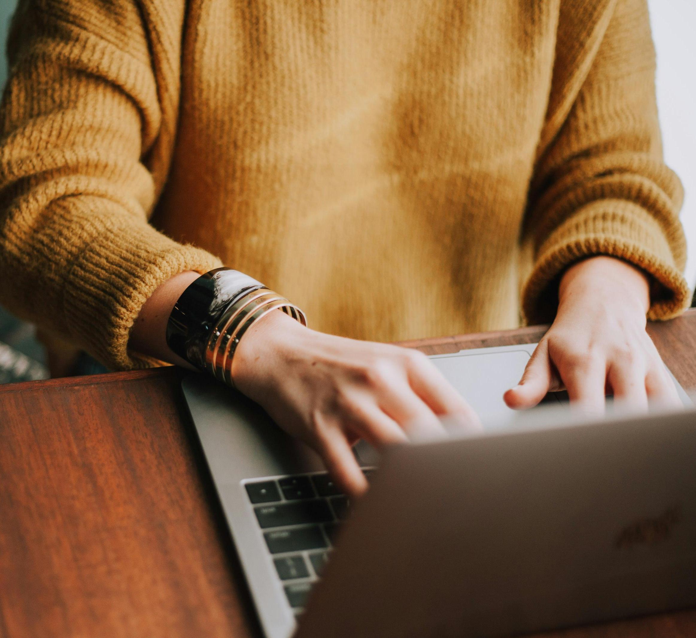 person in a yellow sweater types on a laptop