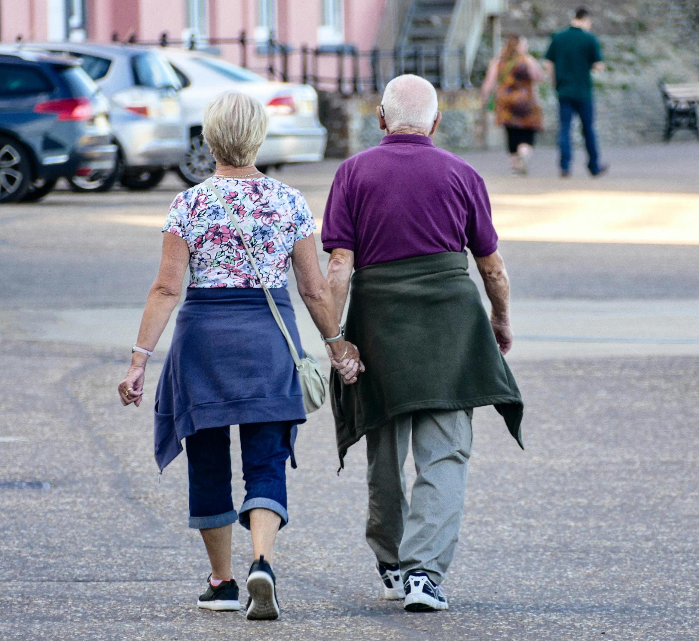 an older adult couple walks hand in hand