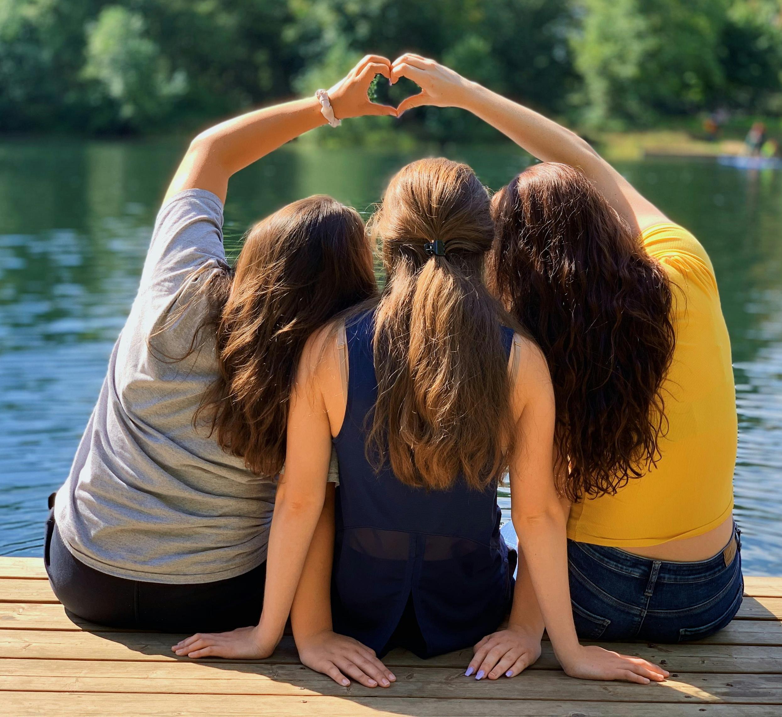 three girls sit together on a dock