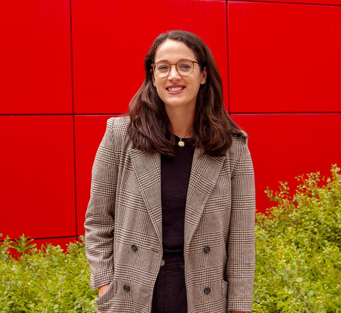 Kathleen McCormick stands in front of a red background and bushes