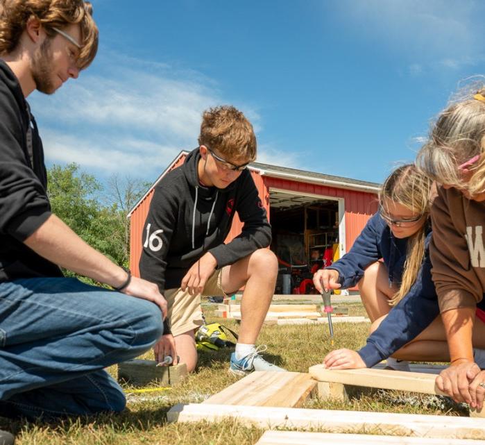 Cornell Cooperative Extension Jefferson County community school coordinator Donna Jean Coleman (right) helps LaFargeville Central School students Alexander Moore (far left), Samuel Duffany and Ella Hunneyman screw together boards on a flower box they built for a student-led community beautification project.
