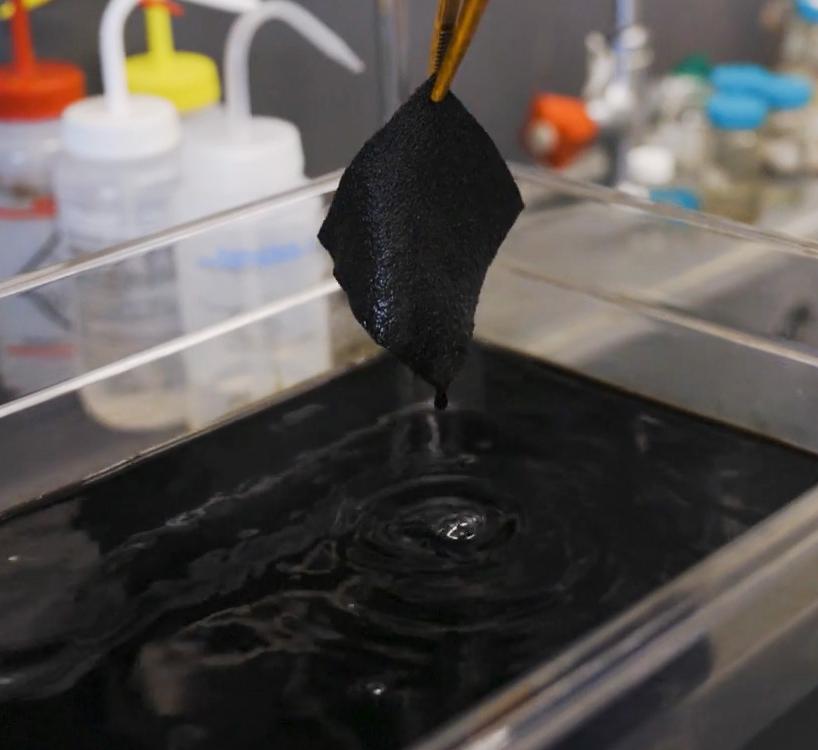 A person pulls a swatch of fabric out of ultrablack dye