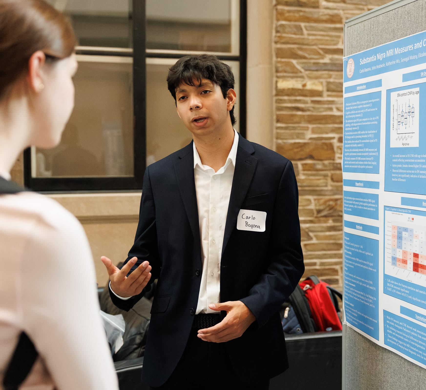 A student discusses their research with a poster next to them.