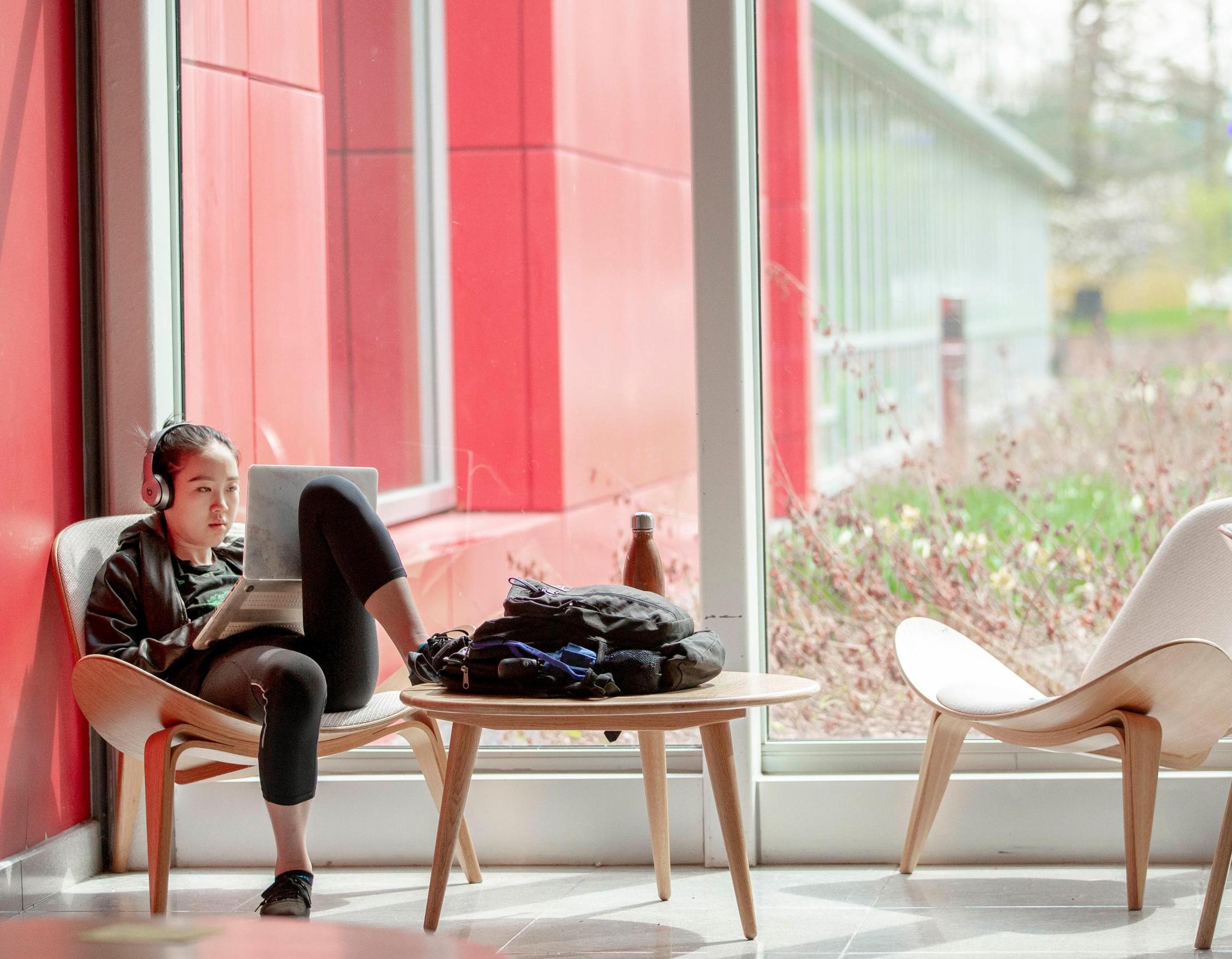 student lounging in a modern chair working on a laptop