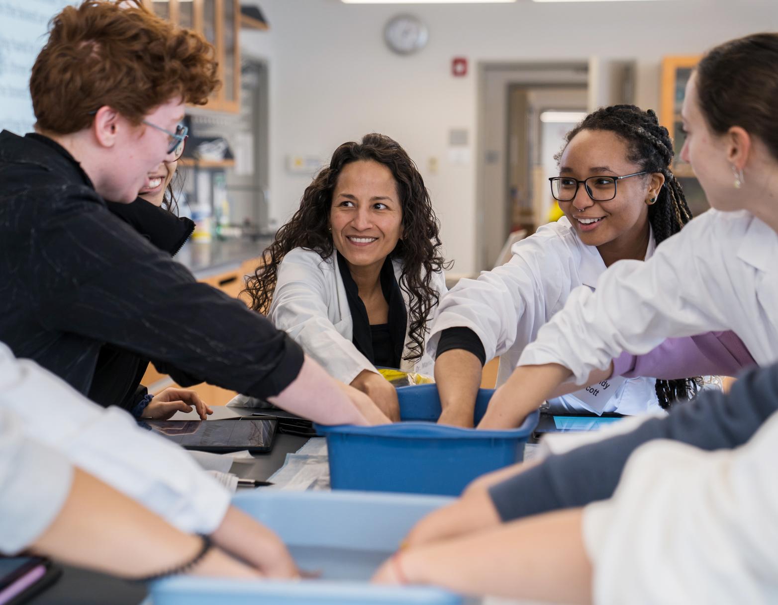 professor and students put their hands in a blue bin in a lab class