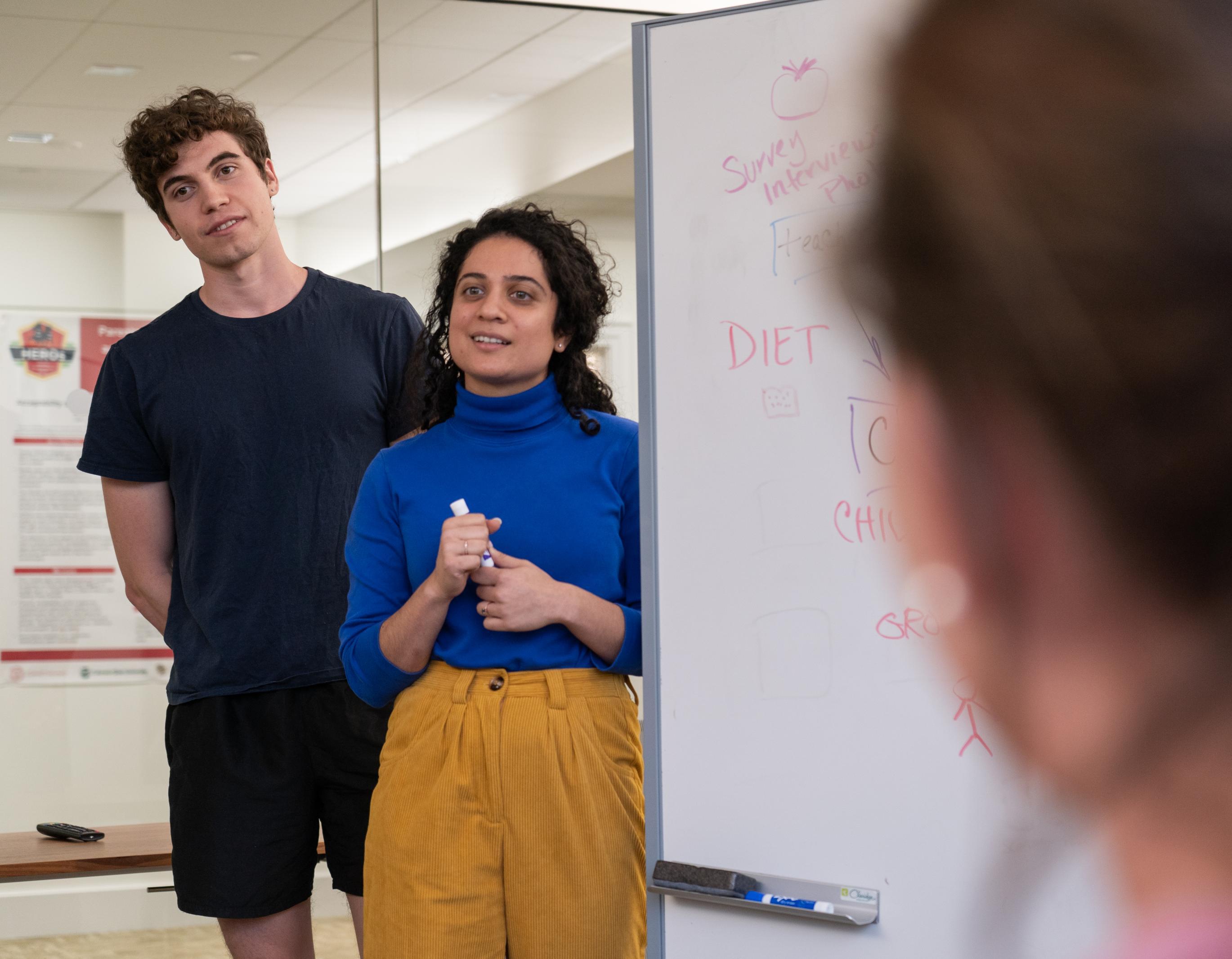 two people standing next to a large white board