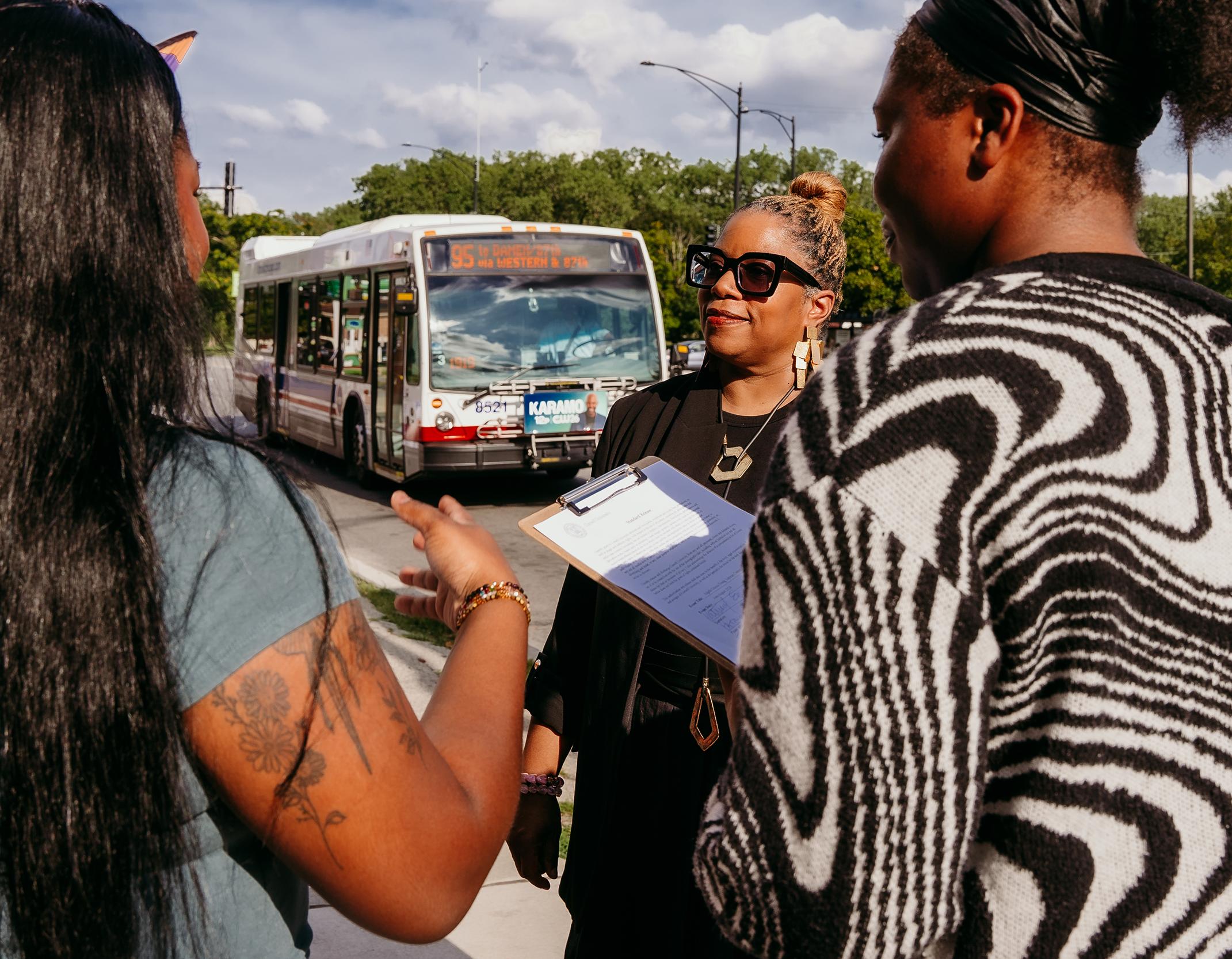 two students and a professor stand talking on a city sidewalk