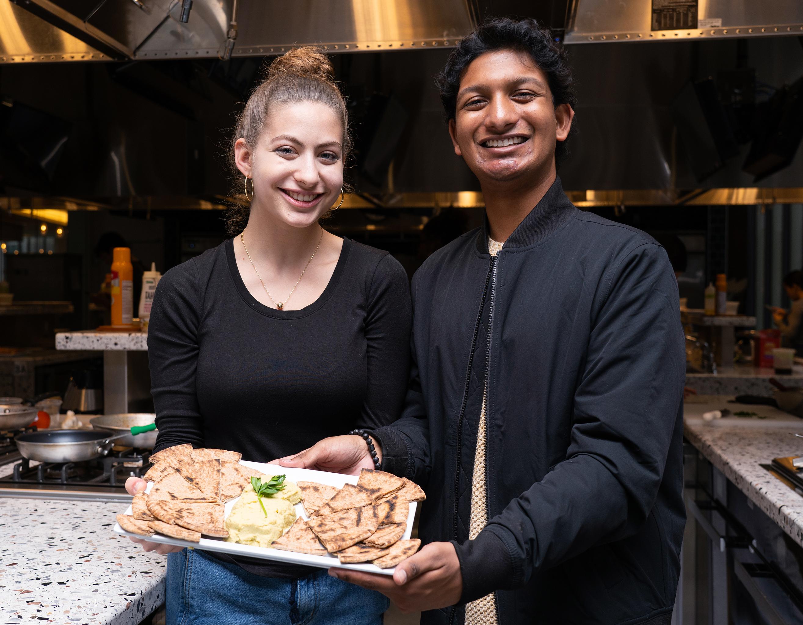 two college students displaying a platter of food in a teaching kitchen