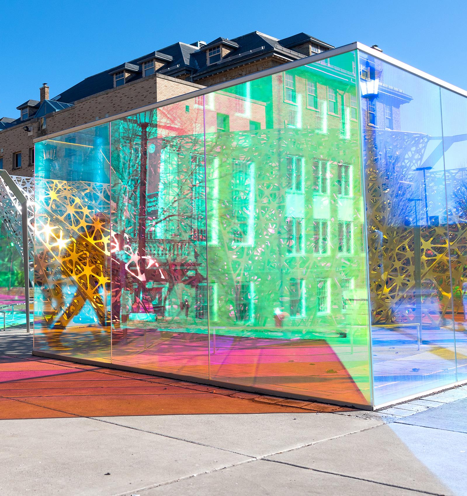 people walking through a large colored glass and metal sculpture