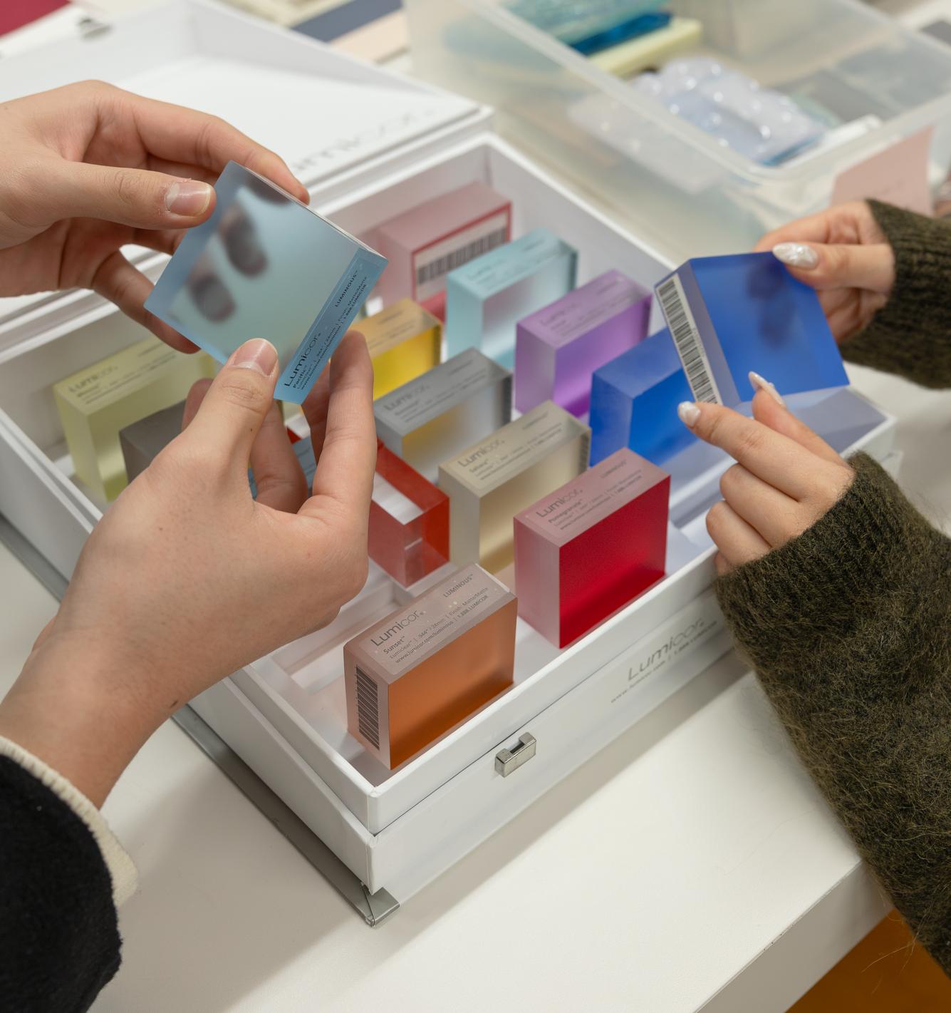 two pairs of hands holding square, colored material samples