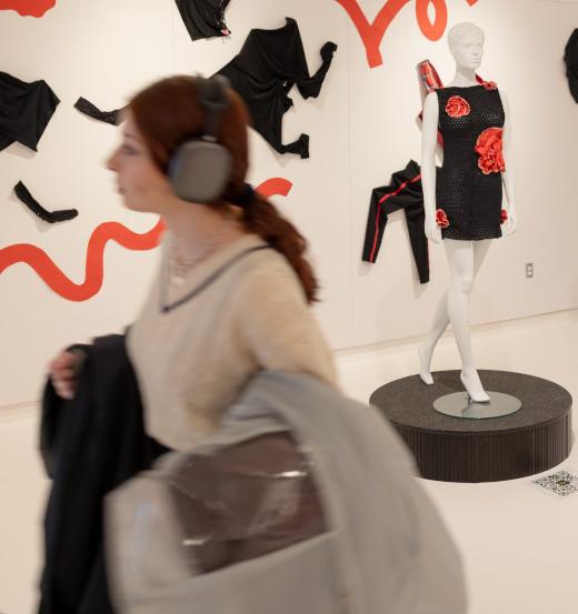 student in headphones walks through a gallery with mannequins