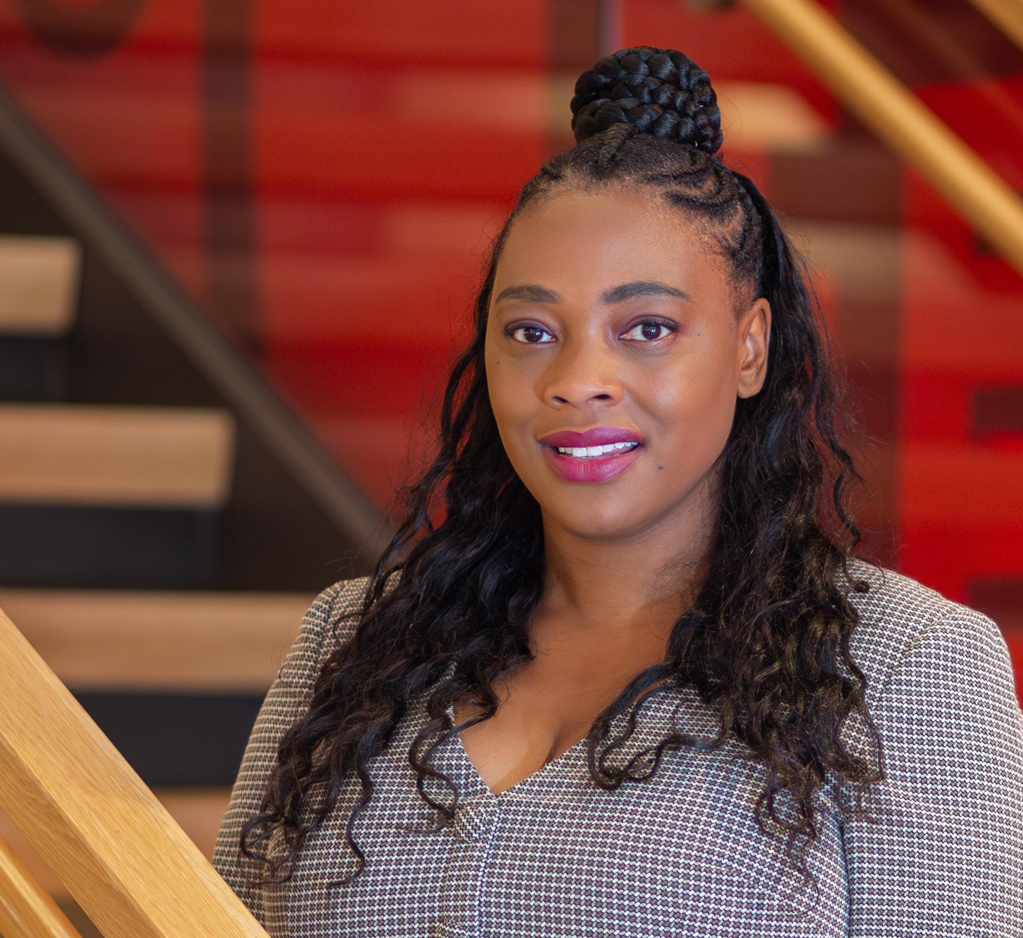 Woman in grey dress standing with a red wall behind her