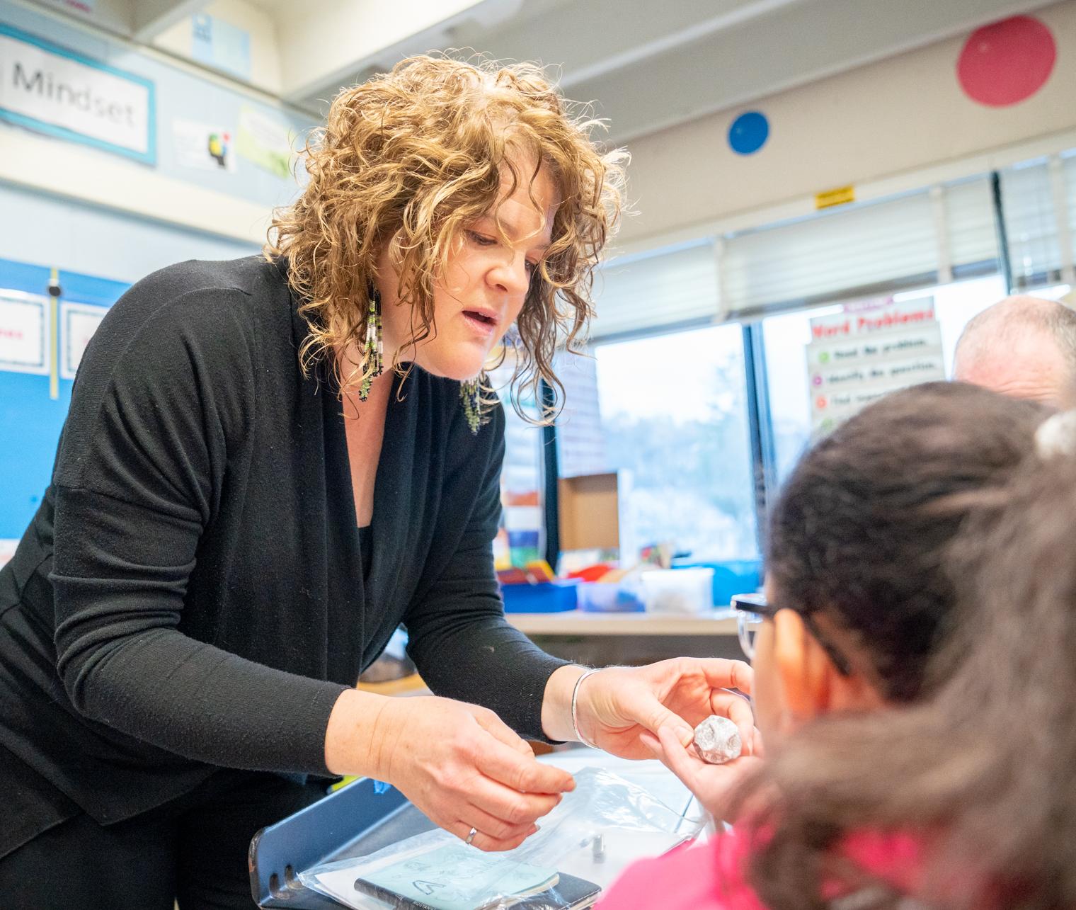 woman leans to talk to elementary school children in a classroom