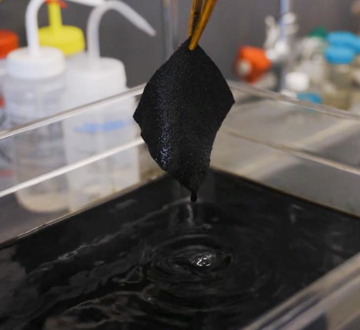 A person pulls a swatch of fabric out of ultrablack dye