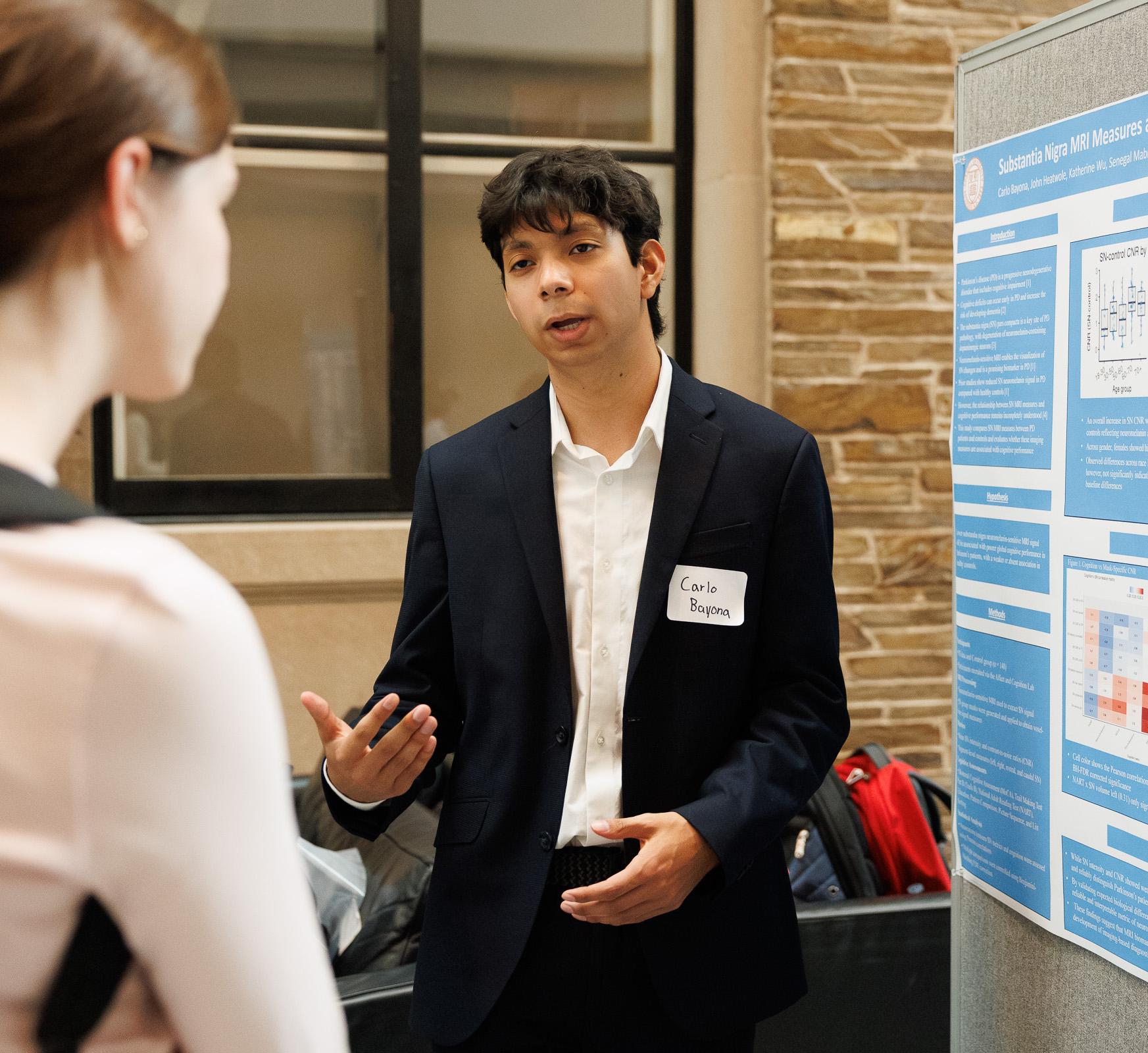 A student discusses their research with a poster next to them.