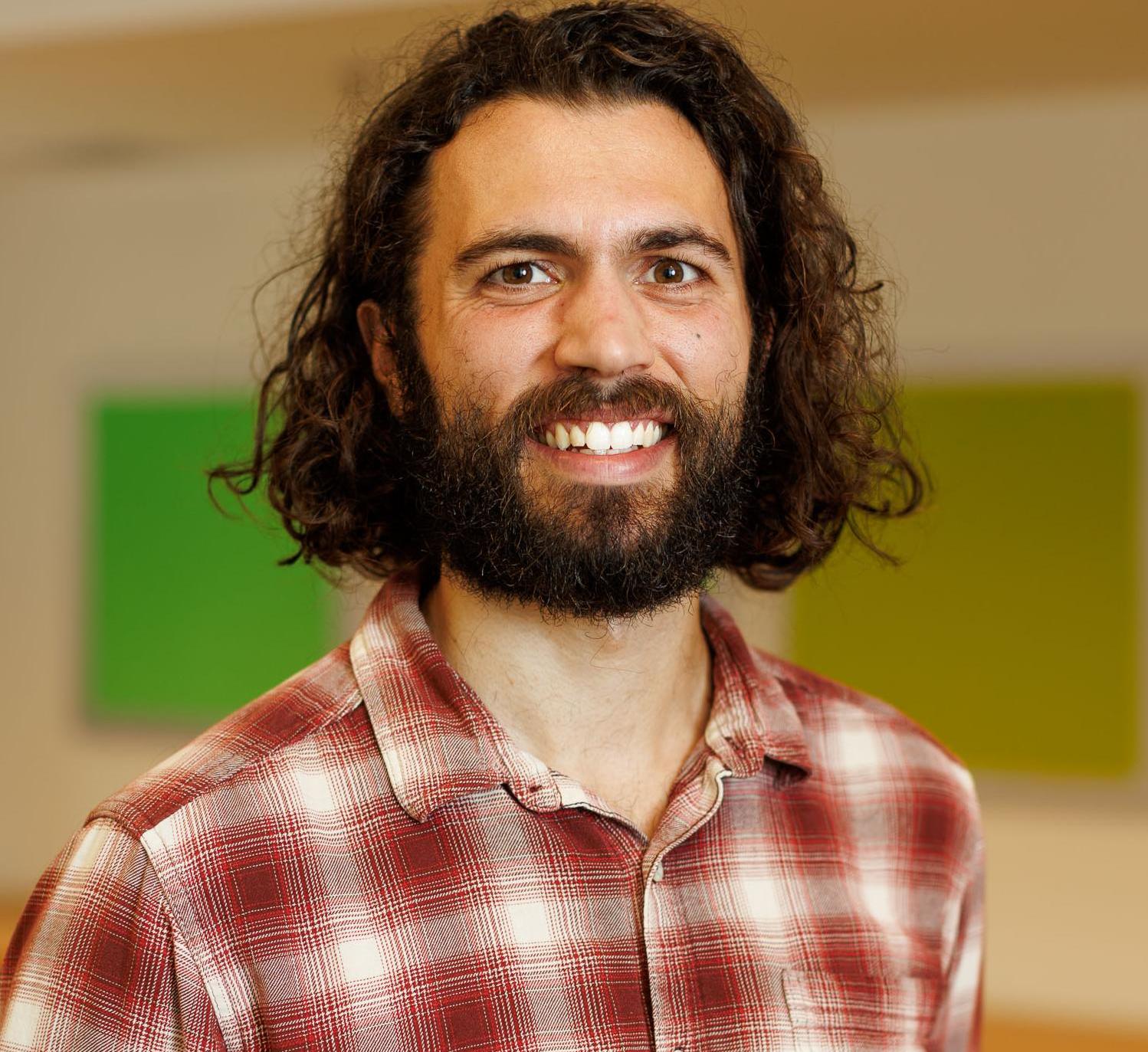 Tim Mateer, wearing a red and white plaid shirt, stands in front of a multi-colored background.