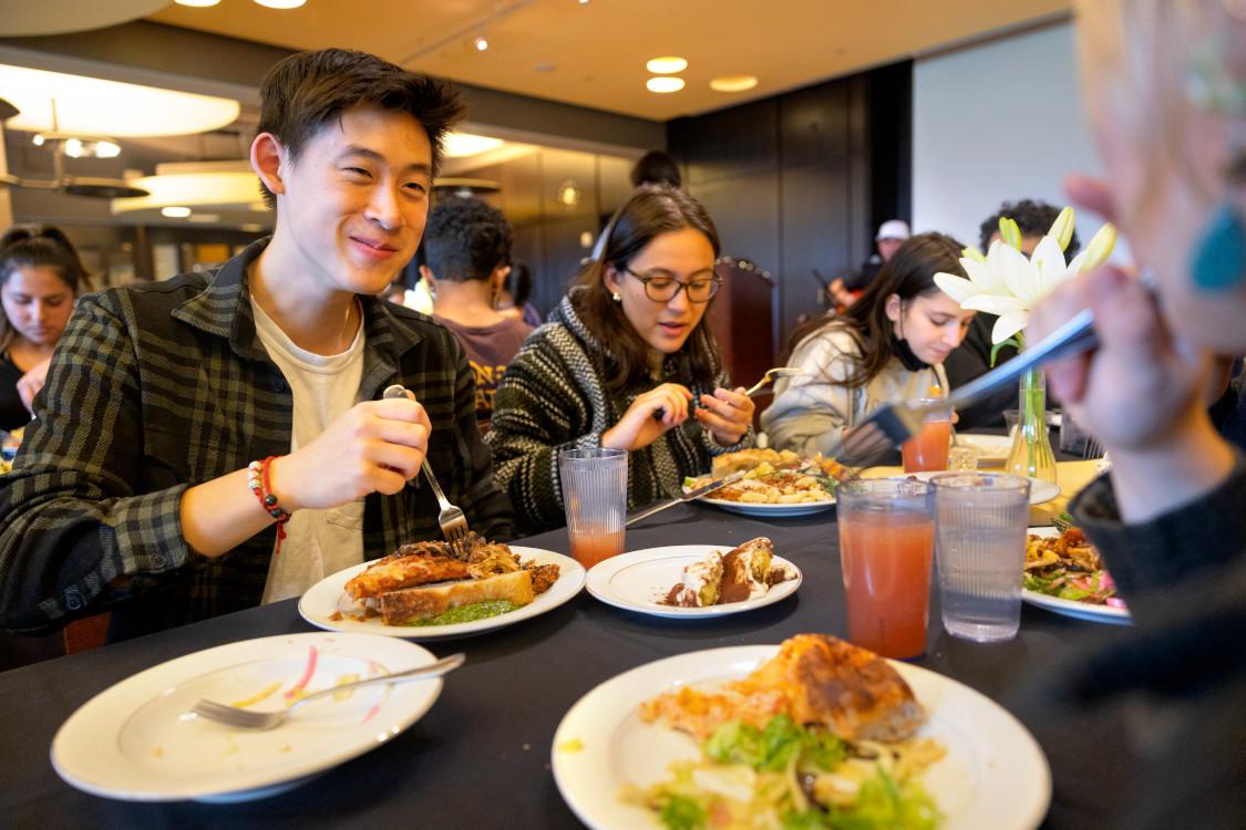 students sitting at a dining hall table eating a meal