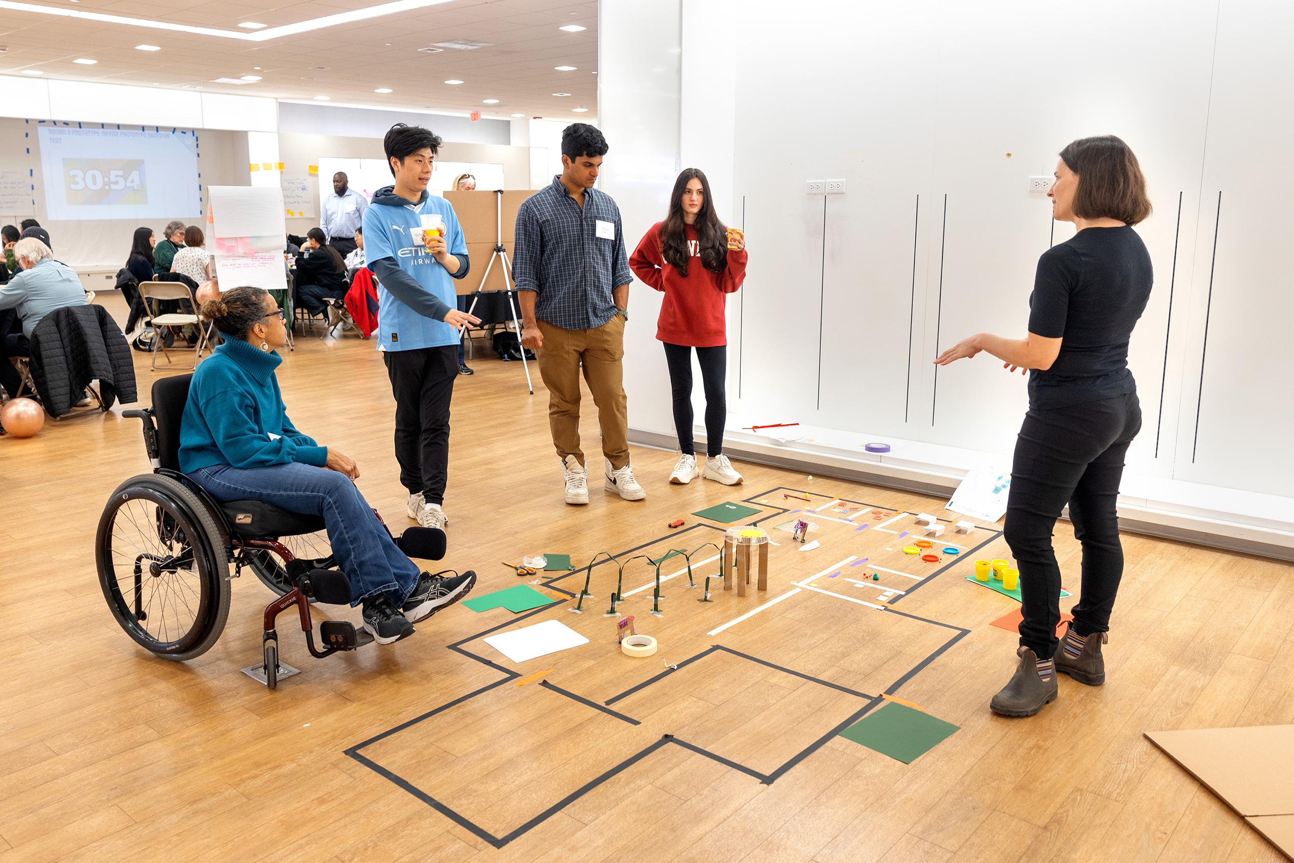 group of people standing around a model of a floorplan on the ground