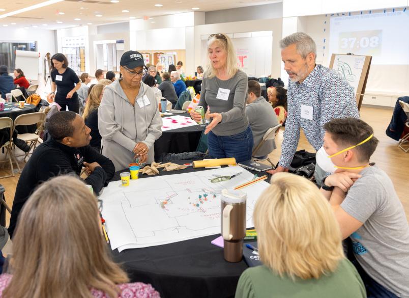 Group of eight individuals discuss plans around a table