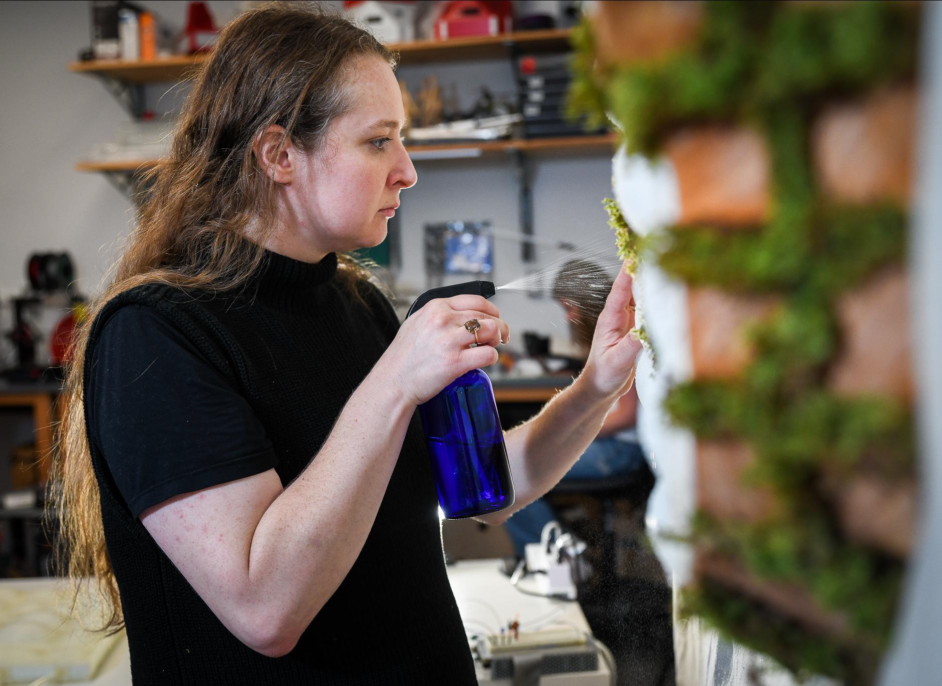 graduate student spraying water on a wall made of moss