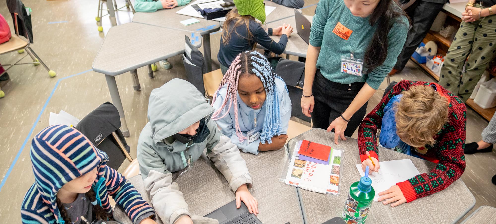 view from above of a group of fourth graders and a Cornell student looking at a computer