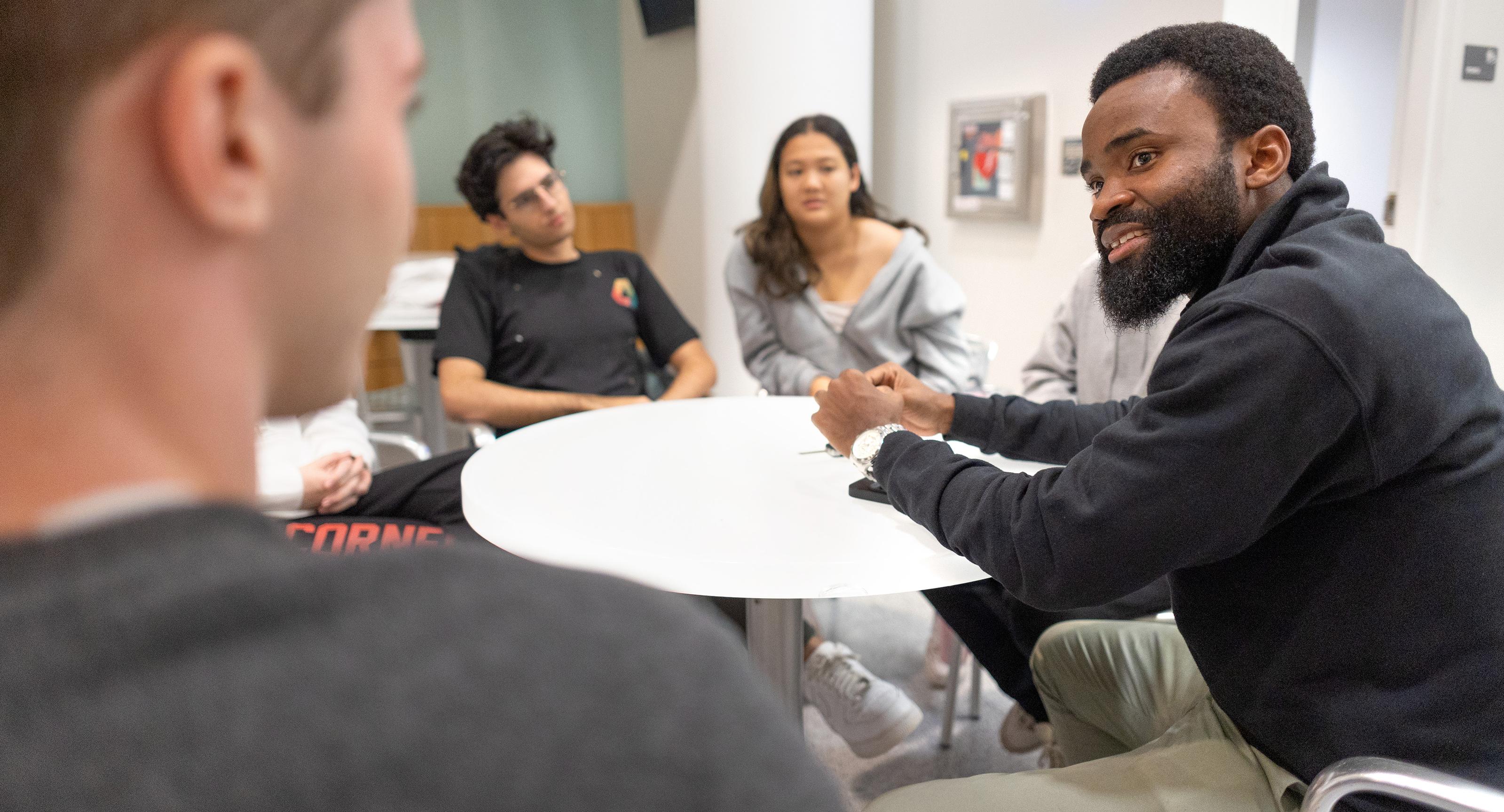 man sitting at a small table with a group of undergraduate students