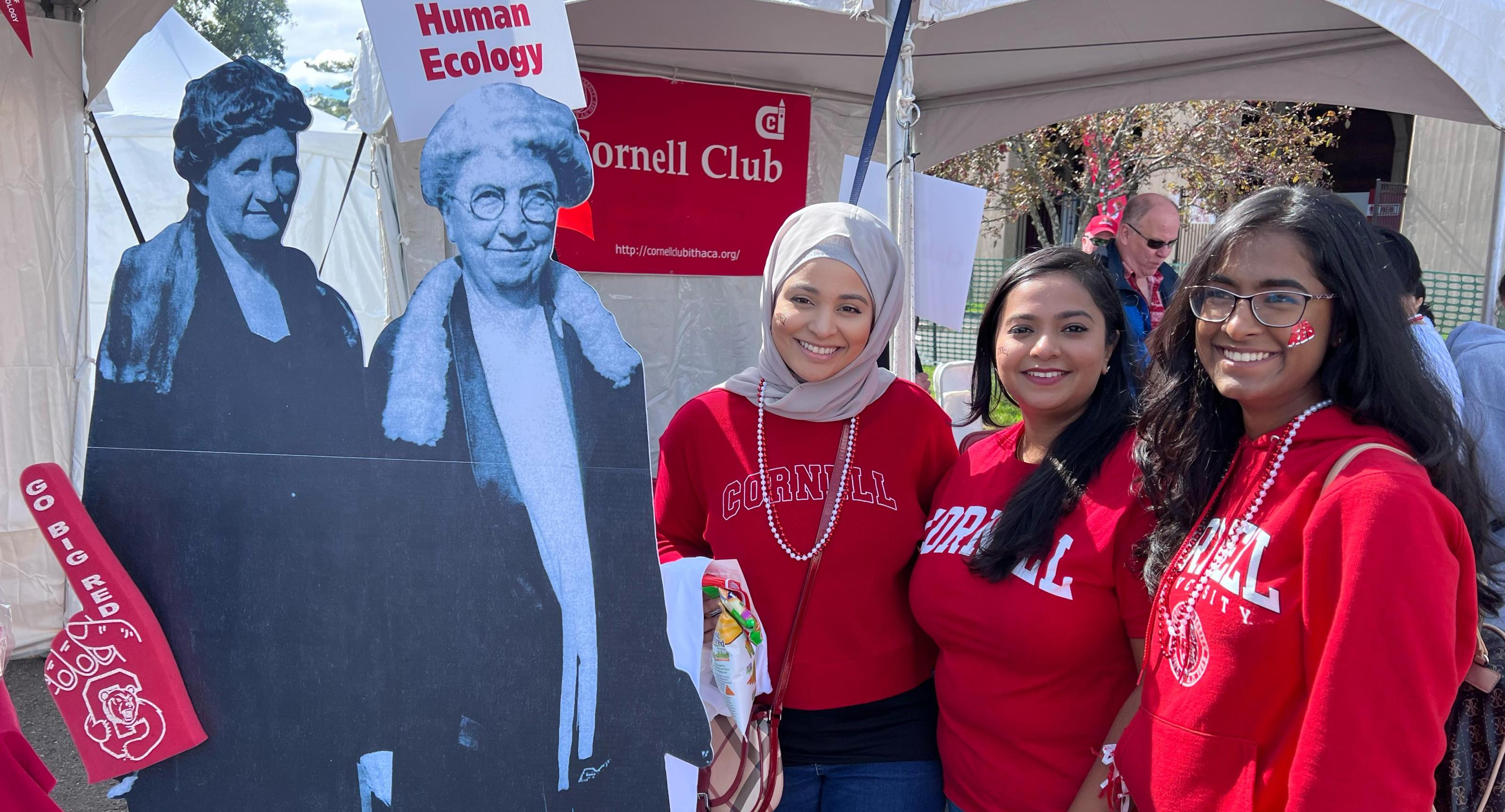 three people in red Cornell sweatshirts stand with black and white cutouts of two women