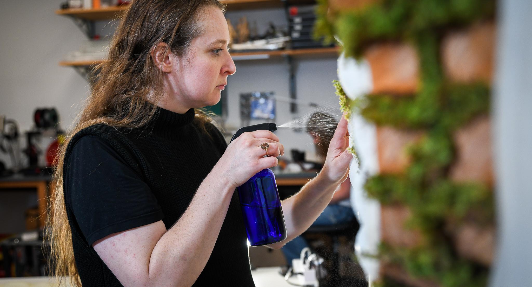 graduate student spraying water on a wall made of moss