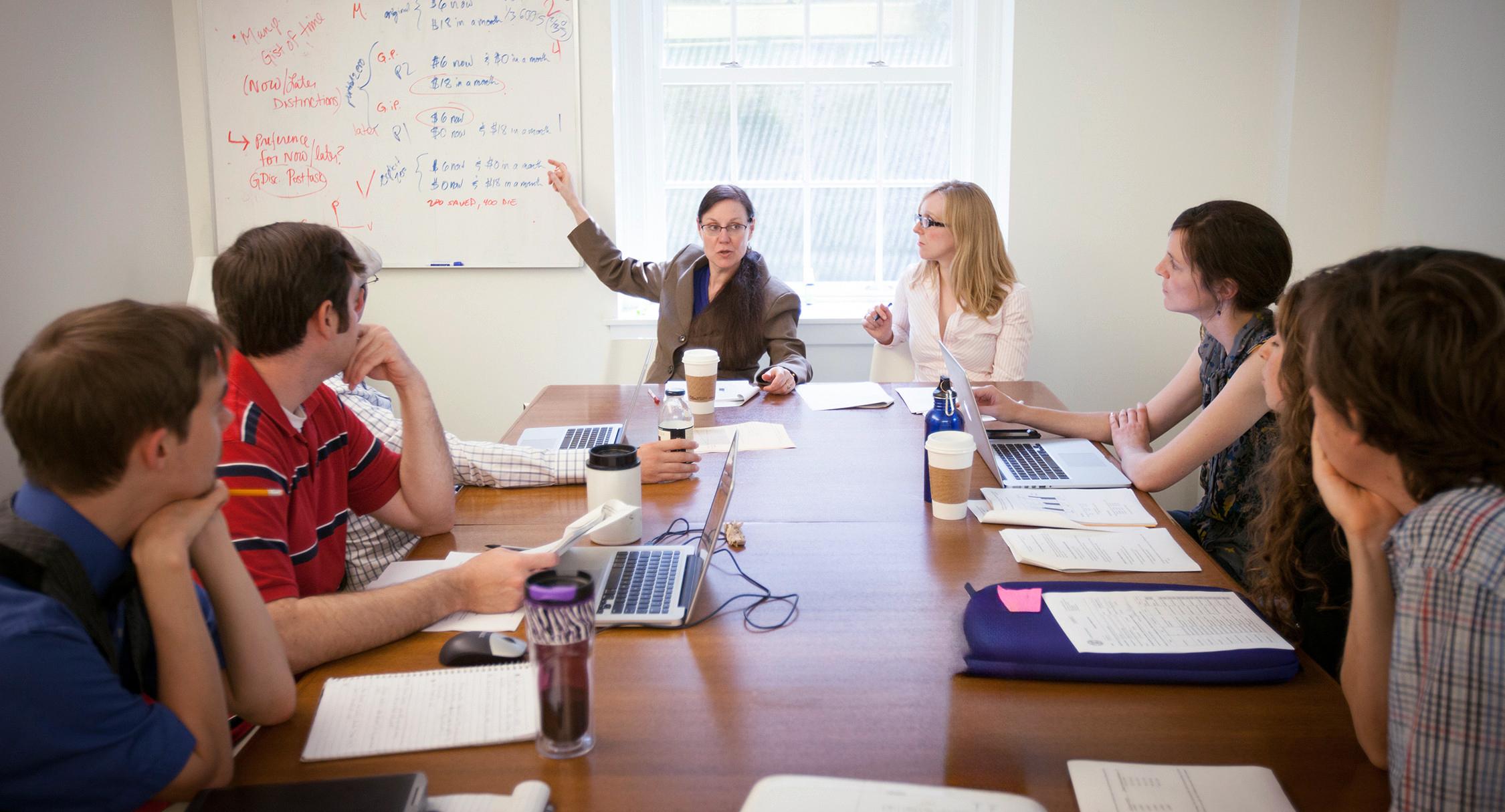 professor pointing at a white board during a meeting at a conference table