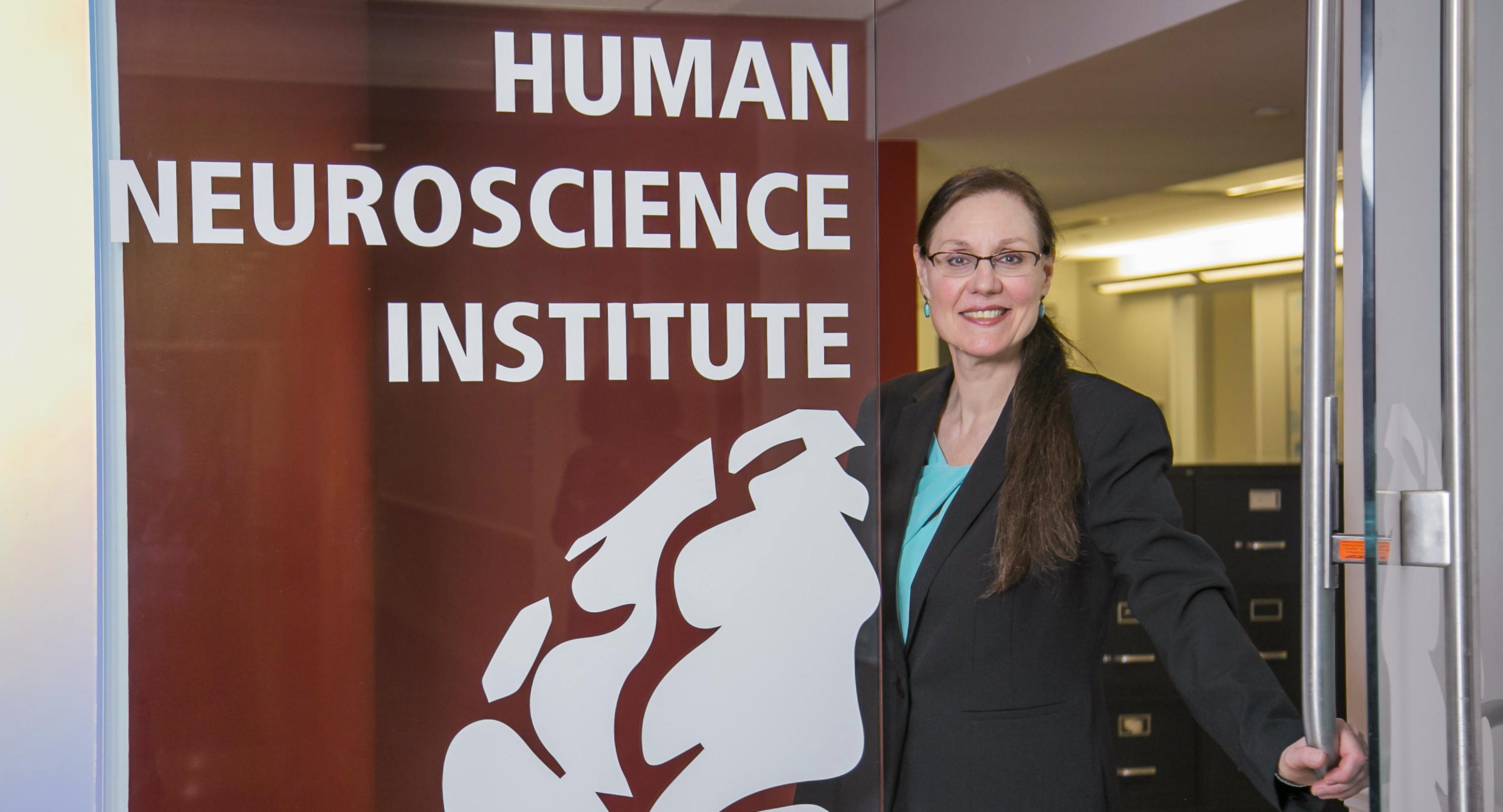 professor opening a glass door next to a wall decal reading "Human Neuroscience Institute" in large white letters
