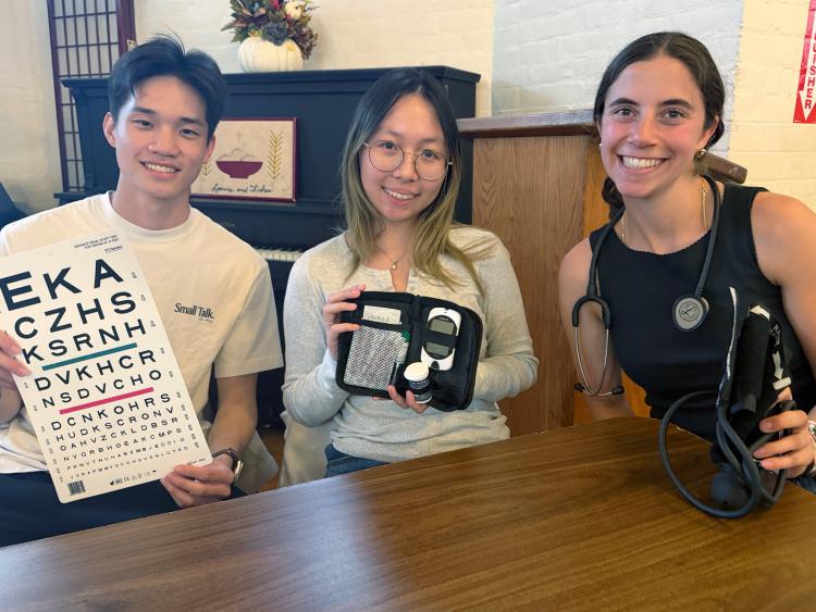 3 students at loaves and fishes hold the blood sugar, eye, and blood pressure tests