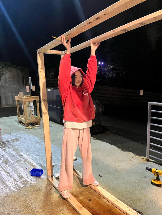 Kate Kim holds up wood as she puts together a pop up story while wearing one of the red Cornellian branded sweatshirts