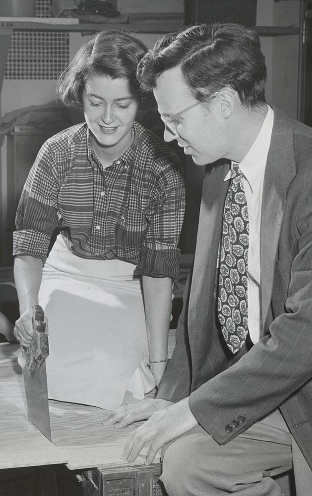 A woman saws a board while the instructor and two fellow students hold the board