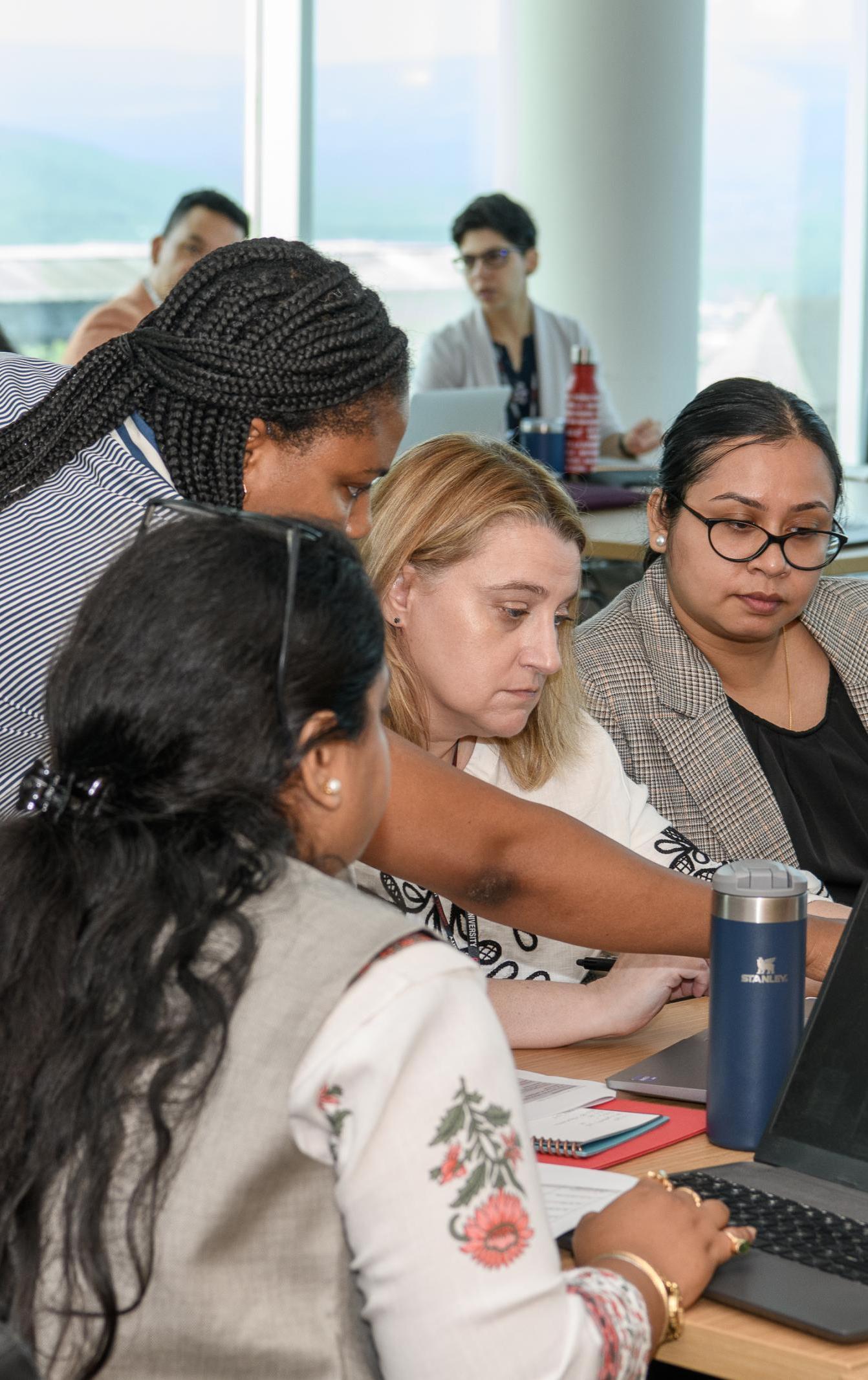 An instructor shows three women how to do something on a computer
