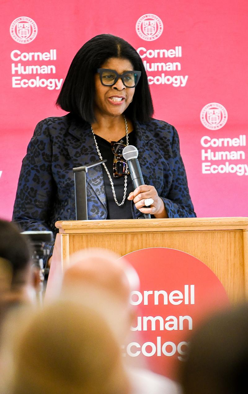 woman wearing glasses standing at a podium speaking to an audience