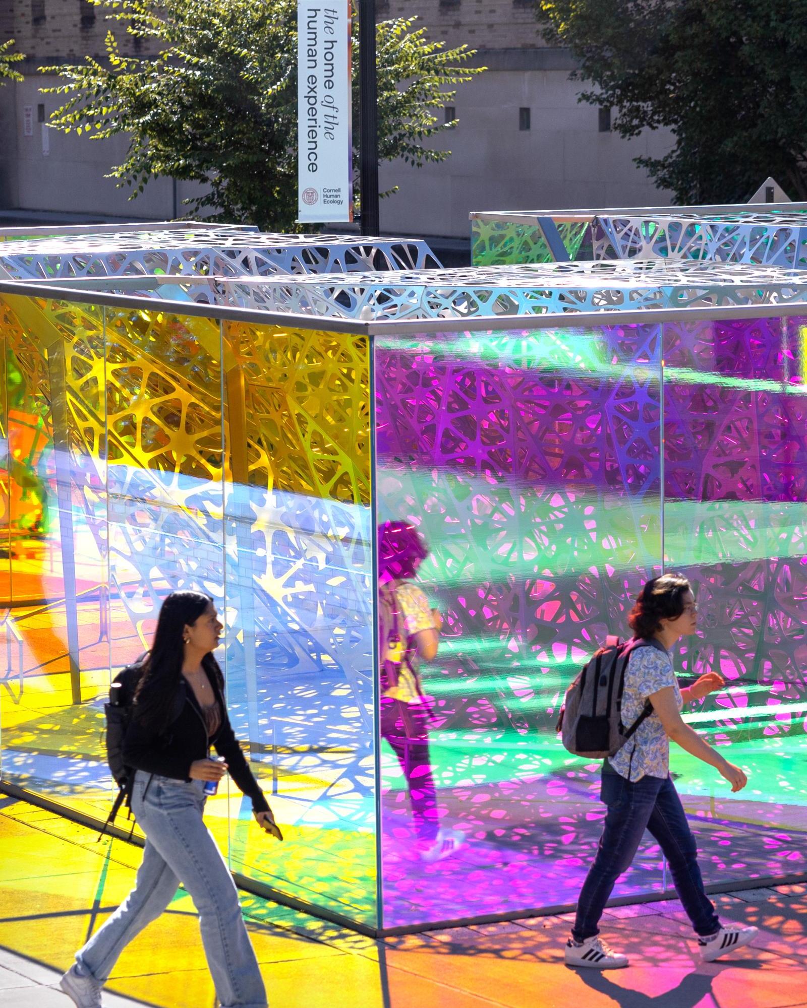2 students walk past the colorful poliform sculpture on a sunny day