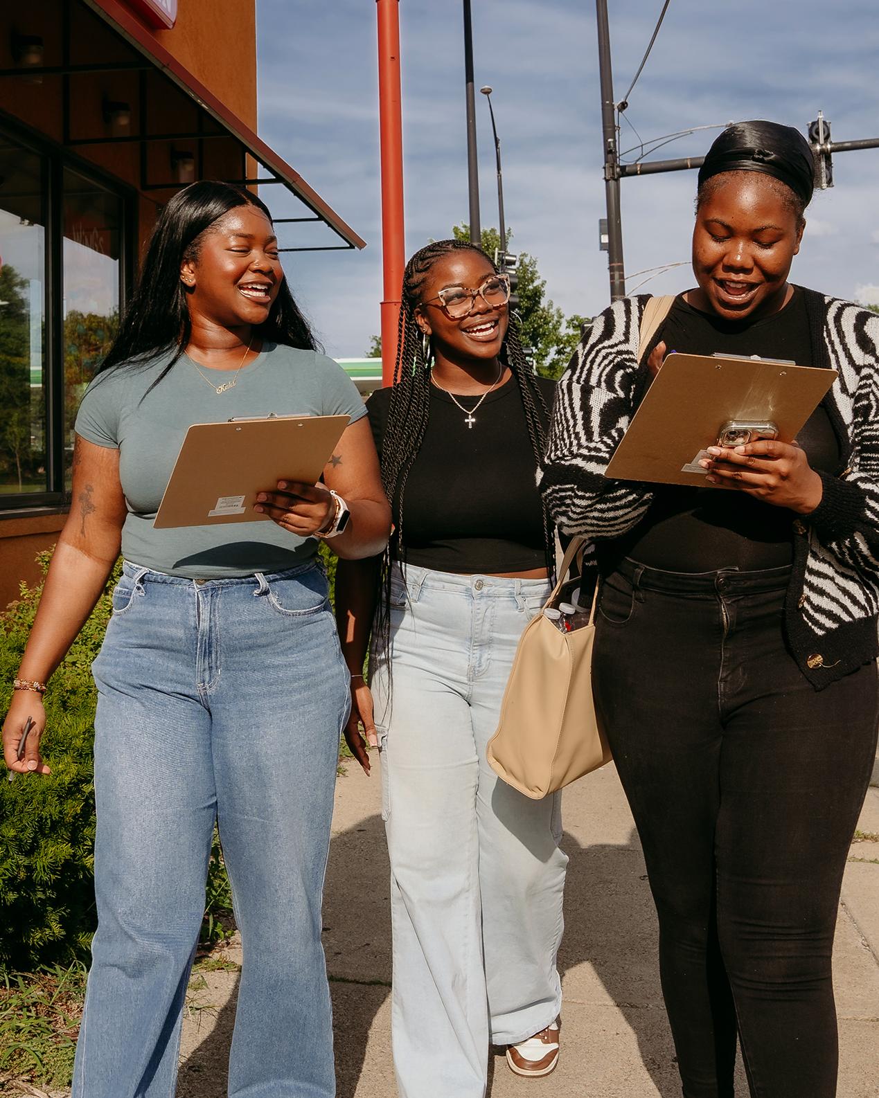 three people walk down a sidewalk outside of a Popeye's restaurant