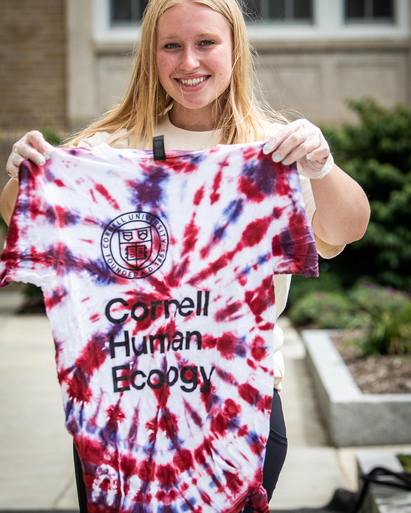 a student holds up a freshly tie dyed tshirt with the words cornell human ecology on it 