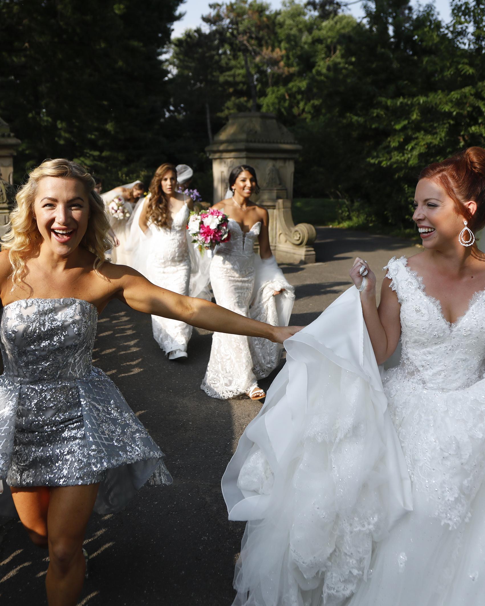 woman in a short, fancy dress with a group of models in briday gowns walk across a bridge